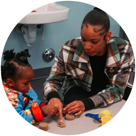 A woman and child play with toys in front of a sink.