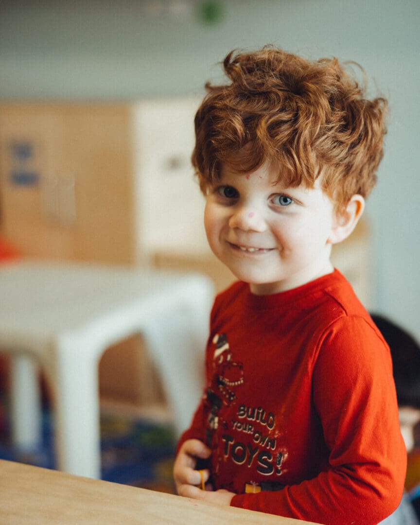 Smiling boy with red hair wearing red shirt.