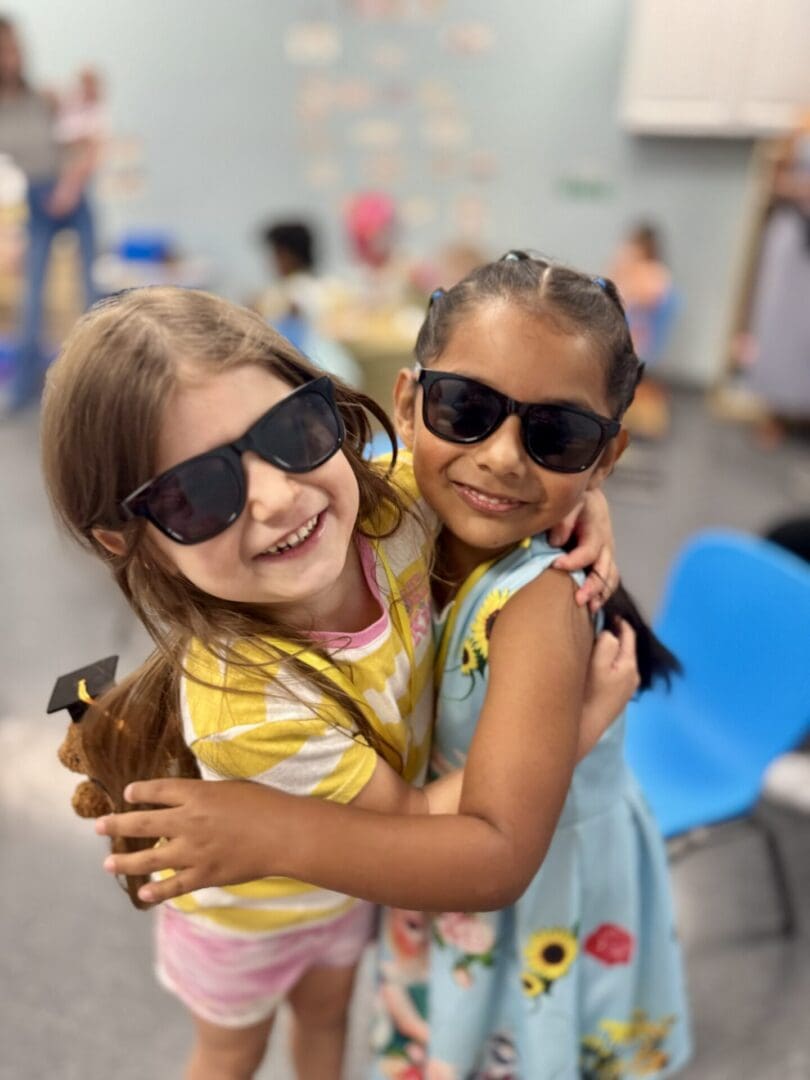 Two girls hugging, wearing sunglasses.