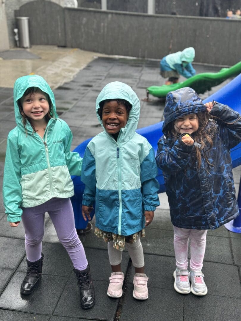 Three kids in raincoats on playground.