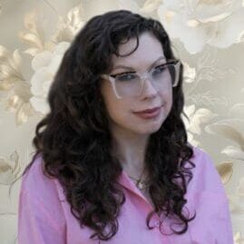 Woman with glasses and curly hair smiling.